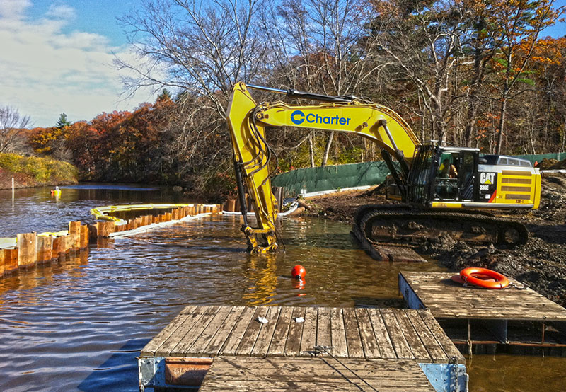 yellow equipment digging in body of water at Medfield State Hospital site