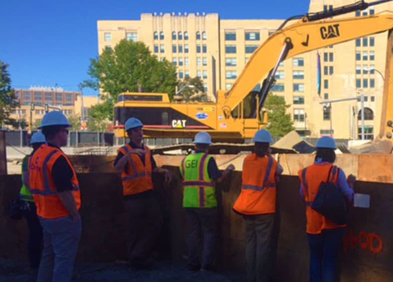 employees by the muddy river excavator in the background